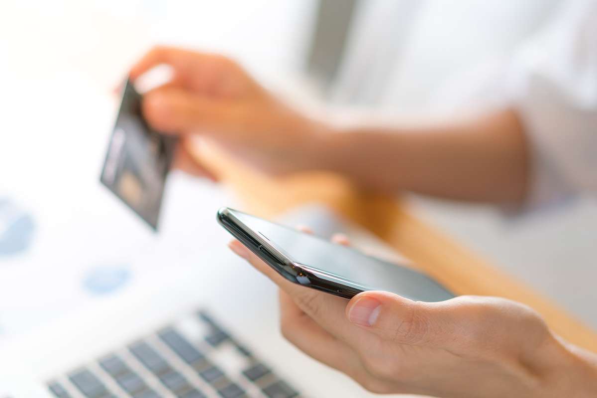 Hands holding a credit card using laptop computer and mobile phone for online shopping .