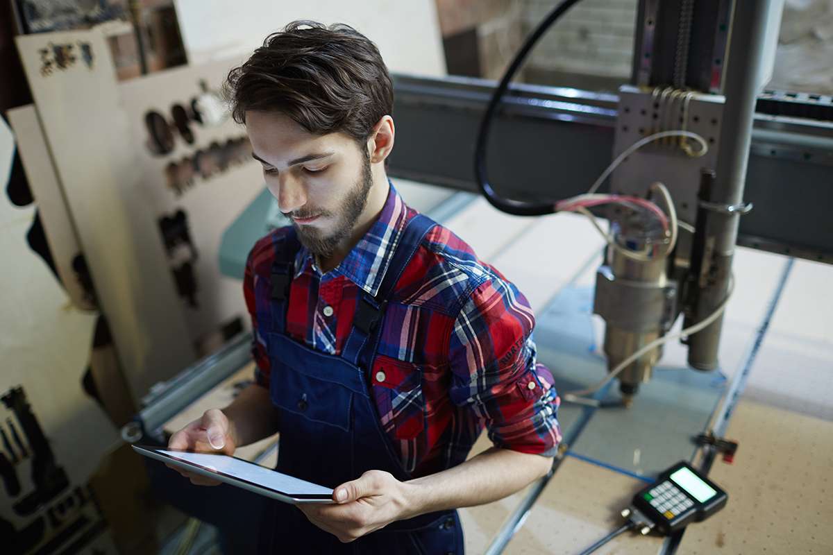 Professional engineer with touchpad standing by lathe-machine