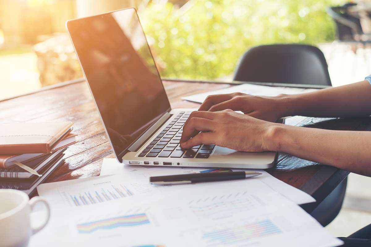 Business woman hand typing on laptop keyboard with Financial charts on the table. Working at her home.